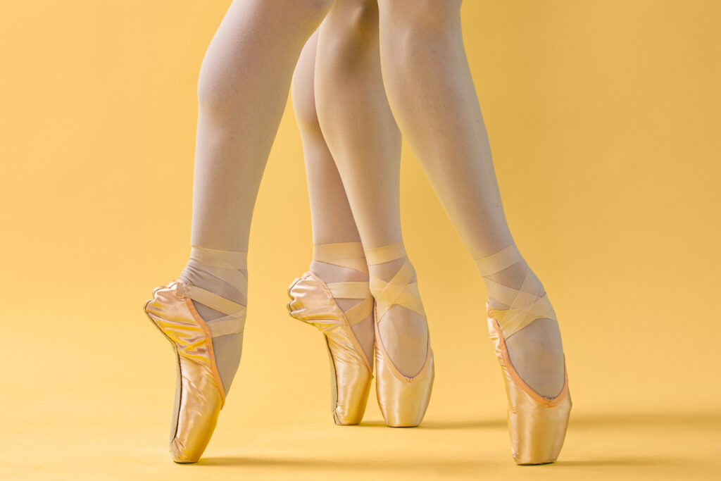 Feet in ballet shoes on point against a yellow background