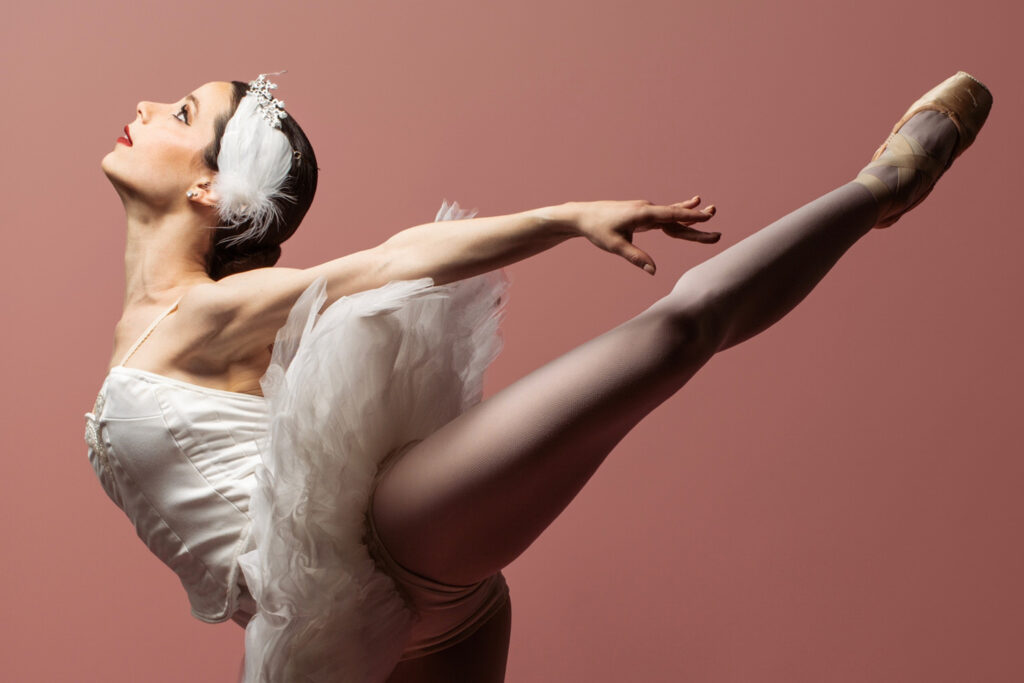 Ballerina doing a pose against a solid pink color background