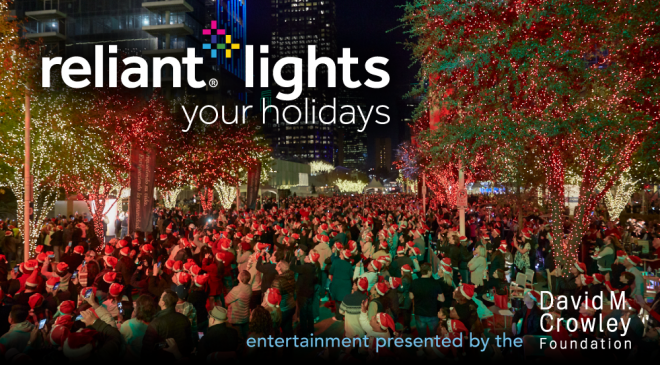 People in Santa hats gather near trees with holiday lights