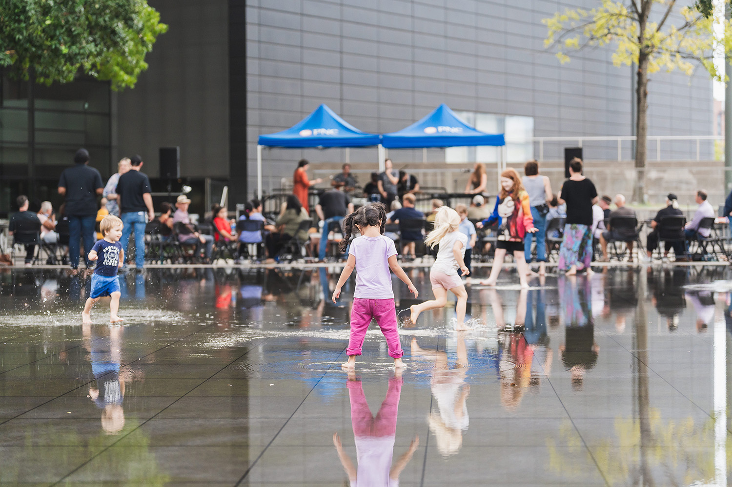 Barefoot children running through water on the pavement at Sammons Park in Dallas.