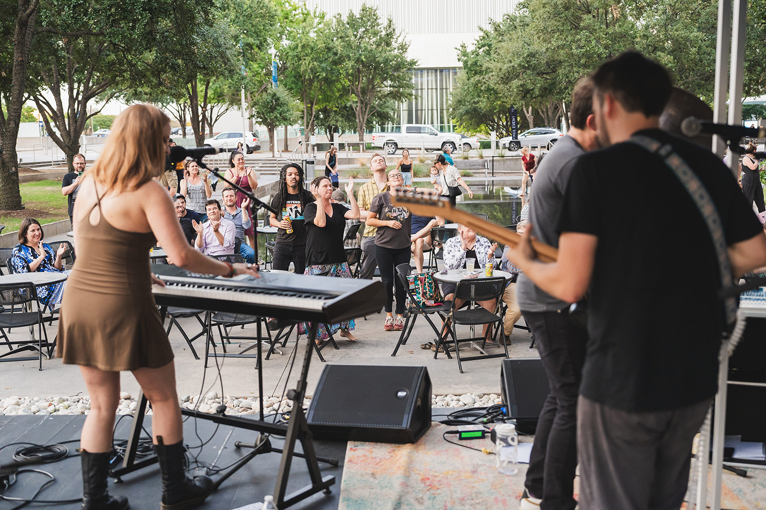 Musicians shown from behind, playing to a small group of people at Sammons Park in Dallas.